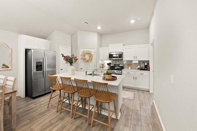 19908 Taggert Dr, Edmond, OK 73012 - kitchen featuring stainless steel appliances, backsplash, white cabinetry, a kitchen breakfast bar, and light wood-type flooring