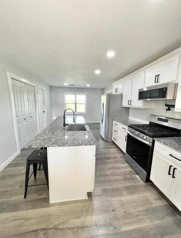 1304 W Walnut St, Tecumseh, OK 74873 - kitchen with stainless steel appliances, wood finished floors, an island with sink, stone countertops, and recessed lighting