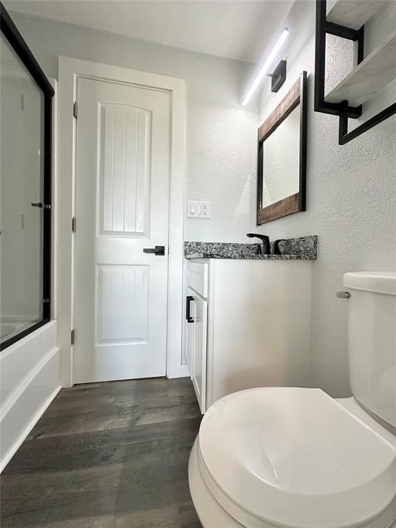 1304 W Walnut St, Tecumseh, OK 74873 - full bathroom with wood finished floors, bath / shower combo with glass door, vanity, and a textured wall