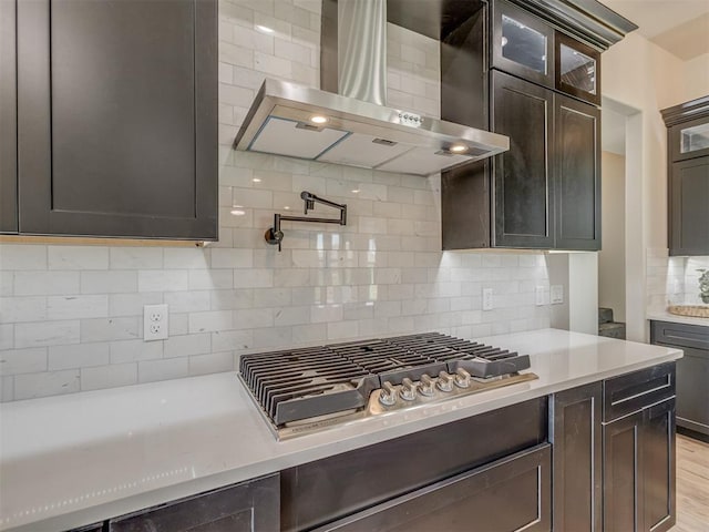 5812 Cimarron Mnr, Guthrie, OK 73044 - kitchen featuring wall chimney exhaust hood, light countertops, backsplash, glass insert cabinets, and stainless steel gas stovetop