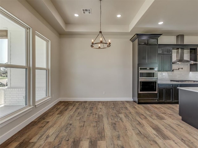 5812 Cimarron Mnr, Guthrie, OK 73044 - kitchen featuring a chandelier, decorative backsplash, wood finished floors, light countertops, and wall chimney range hood