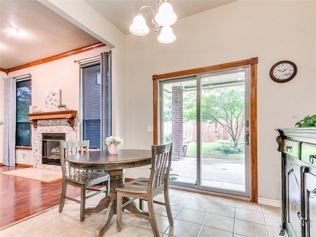 113 Stone Creek Dr, Midwest City, OK 73130 - dining room with light tile patterned flooring, a chandelier, a stone fireplace, baseboards, and crown molding