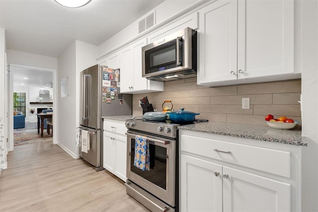 7802 Old Hickory Ln, Oklahoma City, OK 73116 - kitchen with stainless steel appliances, tasteful backsplash, white cabinetry, light wood-style floors, and light stone countertops