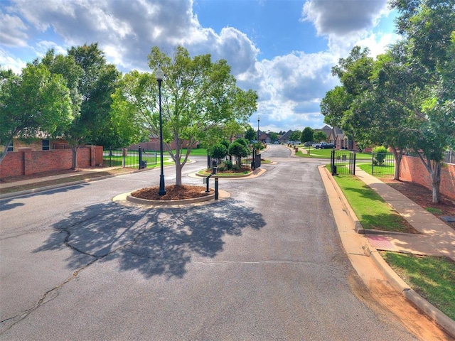 15508 Homecoming Dr, Edmond, OK 73013 - view of asphalt road featuring sidewalks, curbs, street lighting, a gated entry, and a gate