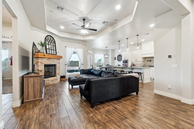 4442 Violet St, Tuttle, OK 73089 - living room with a raised ceiling, a ceiling fan, baseboards, dark wood-style flooring, and a brick fireplace
