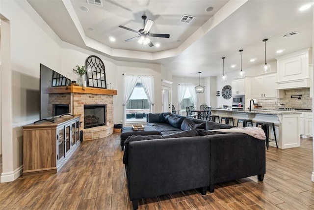 4442 Violet St, Tuttle, OK 73089 - living area featuring a ceiling fan, dark wood-style floors, a raised ceiling, a brick fireplace, and recessed lighting