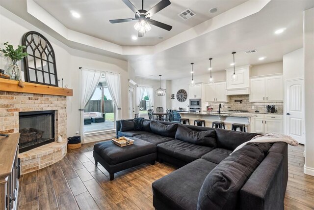 4442 Violet St, Tuttle, OK 73089 - living area with a raised ceiling, a ceiling fan, a brick fireplace, dark wood-style floors, and recessed lighting