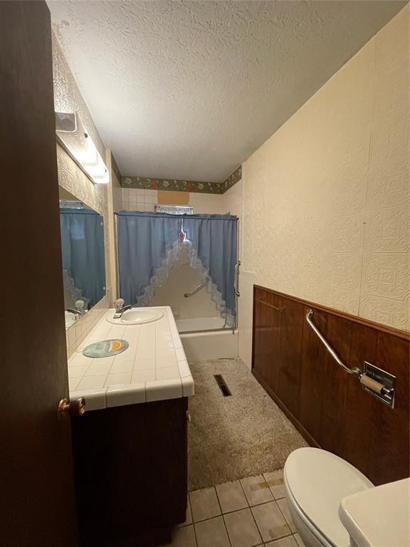 403 NW 3rd St, Minco, OK 73059 - bathroom with vanity, toilet, a textured ceiling, a wainscoted wall, and shower / bath combination with glass door