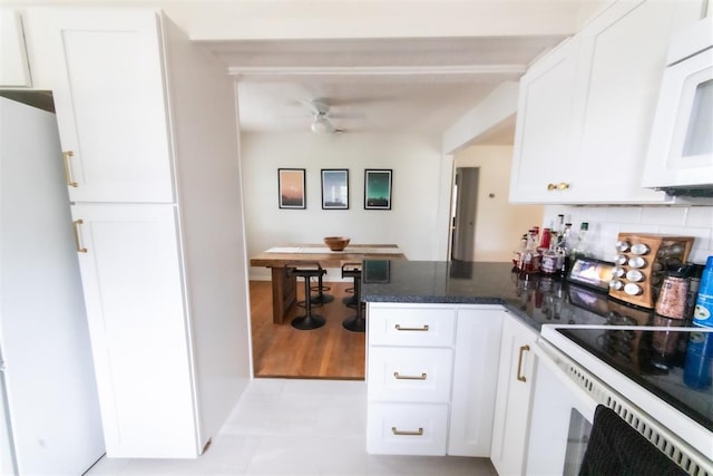 2616 NW 33rd St, Oklahoma City, OK 73112 - kitchen with white appliances, a ceiling fan, white cabinets, a peninsula, and decorative backsplash