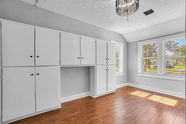 1016 E Cypress St, Altus, OK 73521 - unfurnished bedroom with a textured ceiling, vaulted ceiling, a textured wall, dark wood-type flooring, and multiple windows
