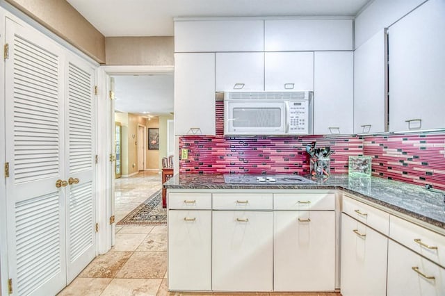 3605 Hampton Ct, Norman, OK 73072 - kitchen with white microwave, electric stovetop, decorative backsplash, dark stone counters, and white cabinetry