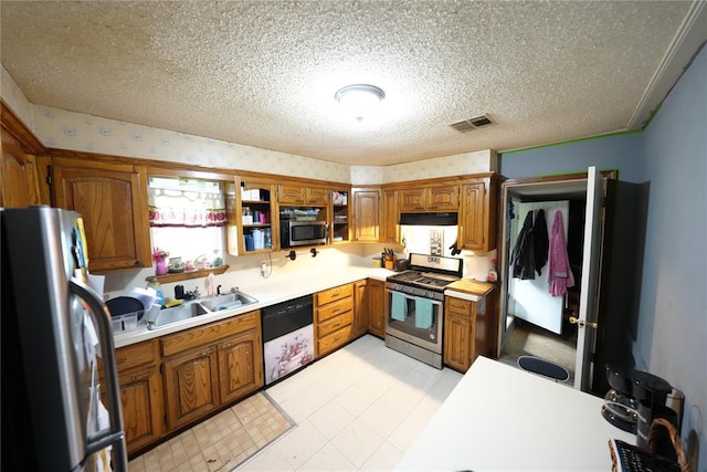 kitchen with appliances with stainless steel finishes, a sink, brown cabinetry, light countertops, and a textured ceiling