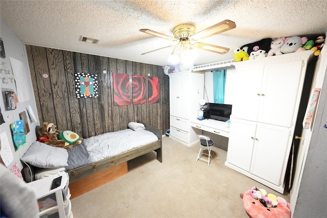 bedroom featuring a desk, light carpet, a textured ceiling, a ceiling fan, and wooden walls