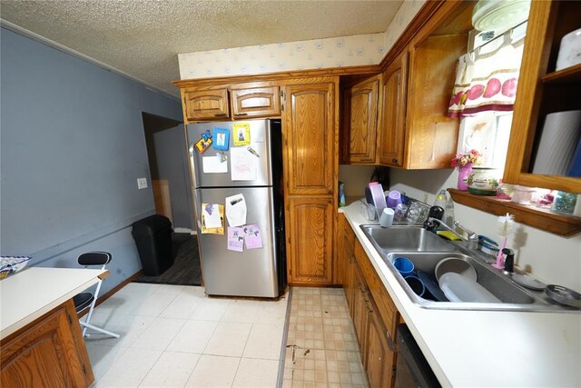kitchen with freestanding refrigerator, brown cabinets, a textured ceiling, a sink, and light flooring