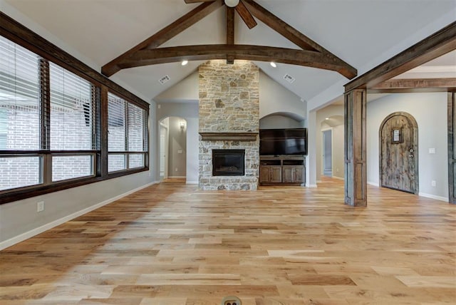 1440 Station St, Edmond, OK 73034 - unfurnished living room featuring arched walkways, beamed ceiling, a ceiling fan, light wood finished floors, and a stone fireplace