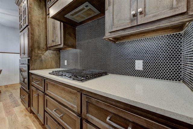 1440 Station St, Edmond, OK 73034 - kitchen featuring stainless steel appliances, light wood-style flooring, light stone counters, range hood, and a wainscoted wall