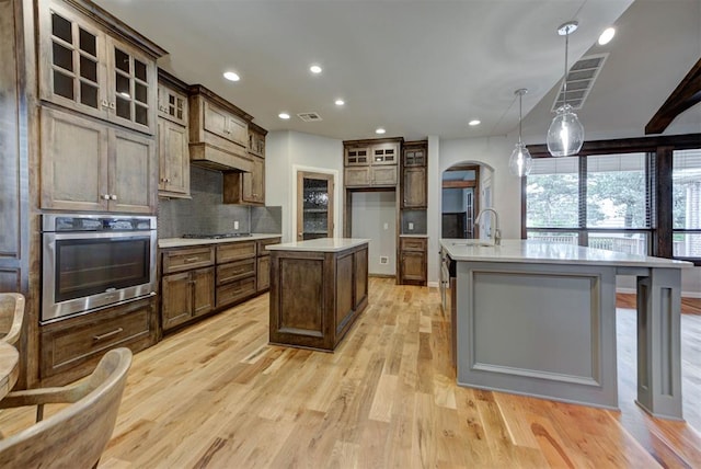 1440 Station St, Edmond, OK 73034 - kitchen with appliances with stainless steel finishes, a center island with sink, light wood-style flooring, tasteful backsplash, and recessed lighting