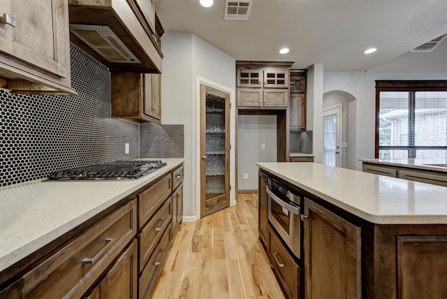 1440 Station St, Edmond, OK 73034 - kitchen featuring stainless steel gas stovetop, arched walkways, light wood-style floors, backsplash, and light countertops