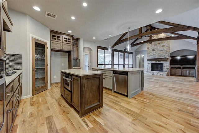 1440 Station St, Edmond, OK 73034 - kitchen featuring appliances with stainless steel finishes, a center island with sink, arched walkways, light wood finished floors, and light countertops