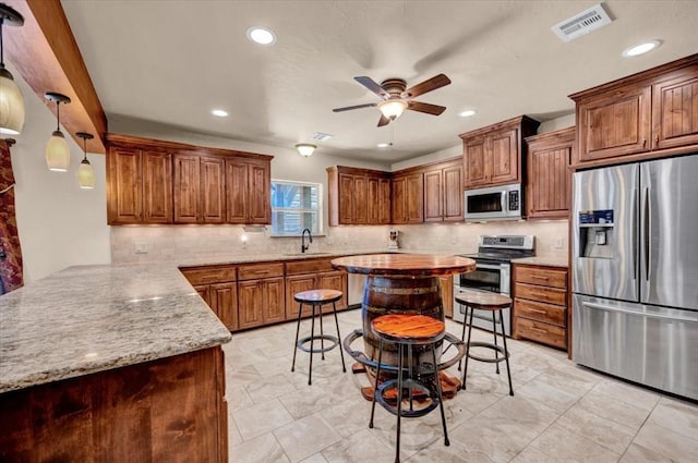 2801 John Deere Ave Unit 1, Edmond, OK 73034 - kitchen with stainless steel appliances, a sink, a ceiling fan, decorative backsplash, and brown cabinets