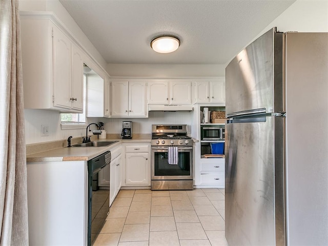 808 Robin Hill Rd, Edmond, OK 73003 - kitchen featuring appliances with stainless steel finishes, a sink, under cabinet range hood, light tile patterned floors, and white cabinetry