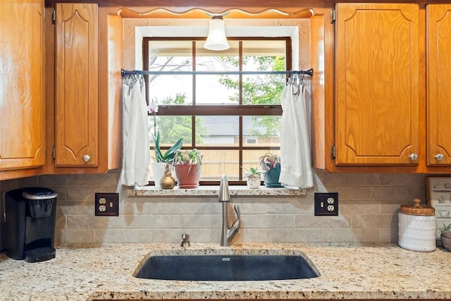2016 Castle Rock, Edmond, OK 73003 - kitchen featuring a sink, backsplash, brown cabinetry, and light stone countertops