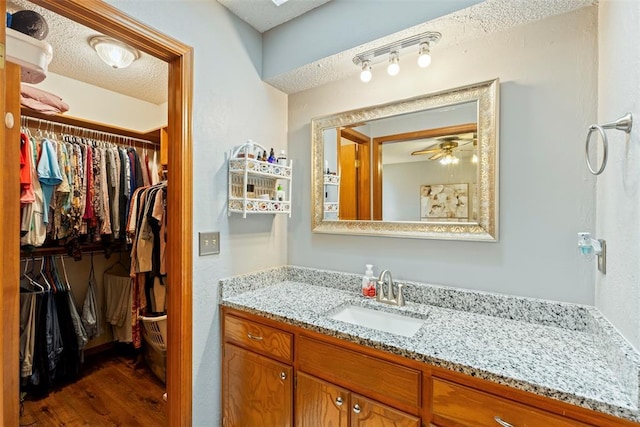 2016 Castle Rock, Edmond, OK 73003 - bathroom with vanity, a textured ceiling, wood finished floors, a ceiling fan, and a walk in closet