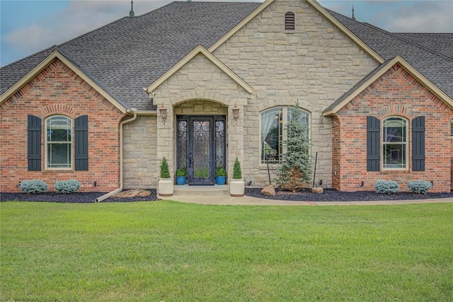 14220 SE 76th Pl, Oklahoma City, OK 73150 - french country home featuring roof with shingles, stone siding, a front yard, and brick siding
