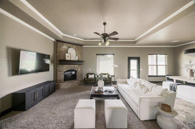 15101 Colonia Bella Dr, Edmond, OK 73013 - carpeted living area featuring a raised ceiling, a ceiling fan, a stone fireplace, and crown molding