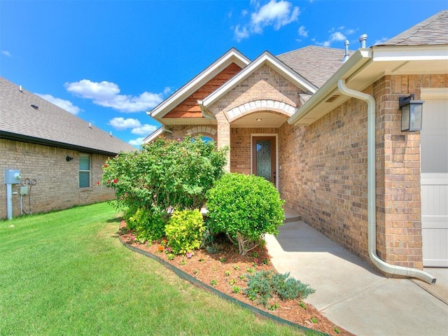 3424 Lakeside Dr, Moore, OK 73160 - view of exterior entry with brick siding, a yard, and roof with shingles