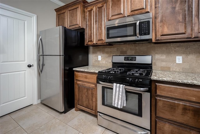 7521 Prairie Twyne Dr, Yukon, OK 73099 - kitchen featuring stainless steel appliances, decorative backsplash, light stone countertops, light tile patterned floors, and crown molding