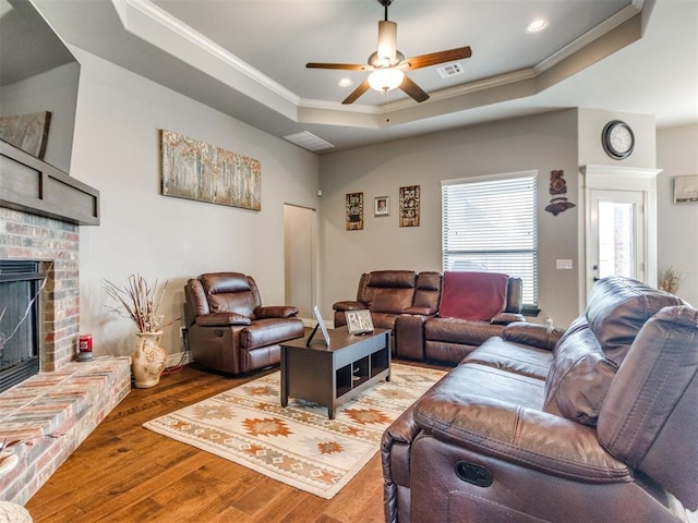 11728 SW 15th Ter, Yukon, OK 73099 - living area with ornamental molding, a tray ceiling, a brick fireplace, ceiling fan, and wood finished floors