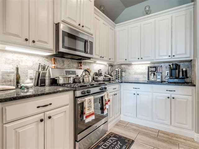 11728 SW 15th Ter, Yukon, OK 73099 - kitchen featuring stainless steel appliances, white cabinets, dark stone countertops, decorative backsplash, and vaulted ceiling
