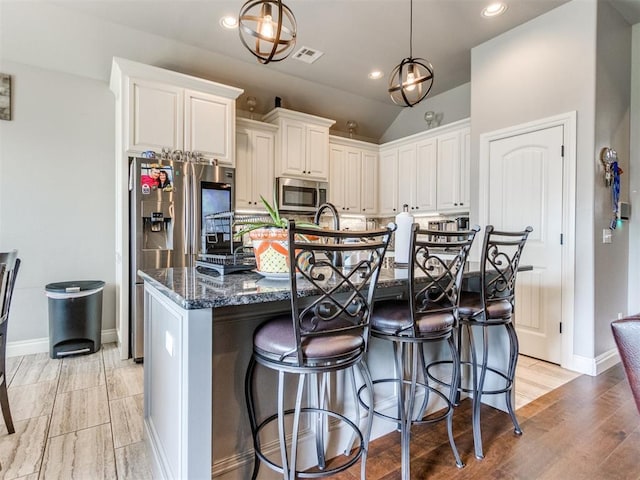 11728 SW 15th Ter, Yukon, OK 73099 - kitchen with appliances with stainless steel finishes, dark stone counters, a center island with sink, vaulted ceiling, and a kitchen bar