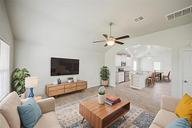 6100 SE 7th St, Midwest City, OK 73110 - living room featuring vaulted ceiling, ceiling fan, arched walkways, light wood-style floors, and baseboards
