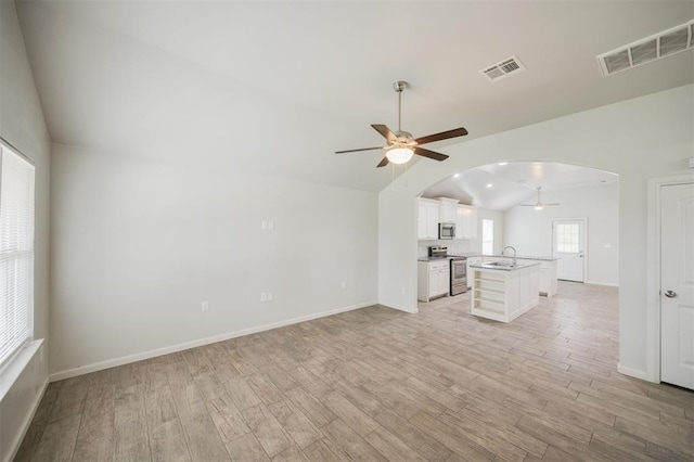 6100 SE 7th St, Midwest City, OK 73110 - unfurnished living room with vaulted ceiling, ceiling fan, light wood-type flooring, arched walkways, and a sink