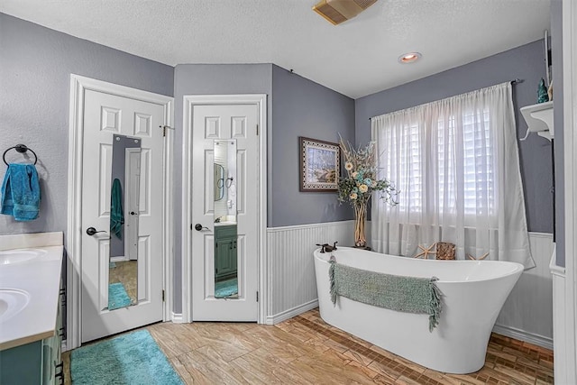 409 Pheasant Cir, Altus, OK 73521 - full bathroom with a textured ceiling, a freestanding tub, double vanity, wood finished floors, and a wainscoted wall