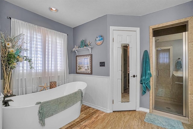 409 Pheasant Cir, Altus, OK 73521 - bathroom with wood finished floors, wainscoting, a soaking tub, and a shower stall