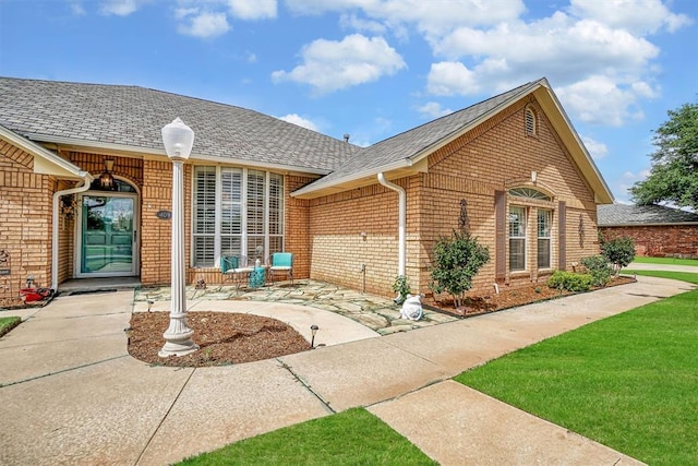 409 Pheasant Cir, Altus, OK 73521 - doorway to property with brick siding, a shingled roof, and a patio area