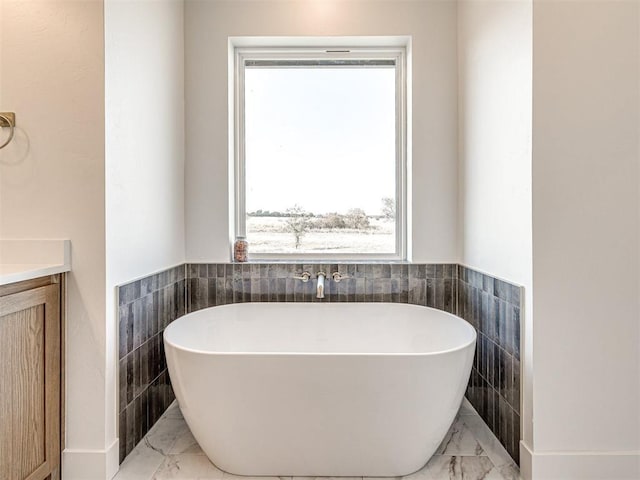 13133 Ashlyn Ln, Yukon, OK 73099 - full bathroom featuring marble tiled floors, tile walls, a freestanding bath, wainscoting, and vanity