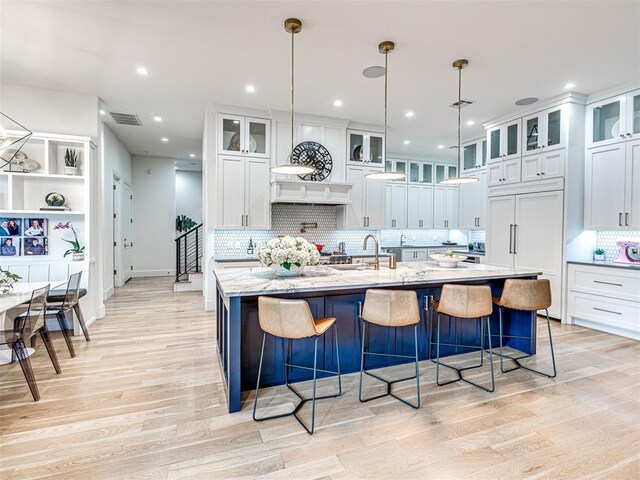 15825 Lacebark Ln, Edmond, OK 73013 - kitchen featuring light wood-style flooring, a spacious island, backsplash, white cabinets, and a breakfast bar