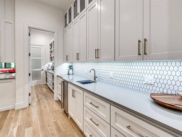 15825 Lacebark Ln, Edmond, OK 73013 - kitchen with a sink, decorative backsplash, light wood-style flooring, light countertops, and glass insert cabinets