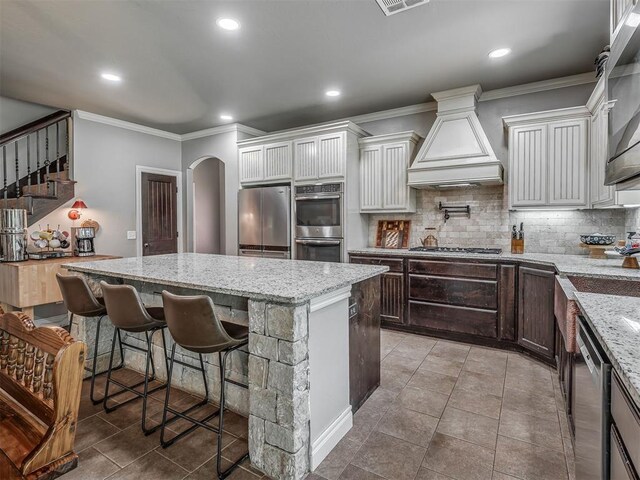 13505 Shady Pine Cir, Edmond, OK 73025 - kitchen with stainless steel appliances, premium range hood, ornamental molding, arched walkways, and a center island