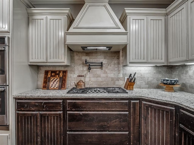 13505 Shady Pine Cir, Edmond, OK 73025 - kitchen featuring stainless steel gas cooktop, custom exhaust hood, tasteful backsplash, light stone countertops, and ornamental molding