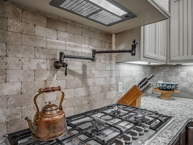 13505 Shady Pine Cir, Edmond, OK 73025 - kitchen featuring stainless steel gas cooktop, light stone counters, exhaust hood, and concrete block wall
