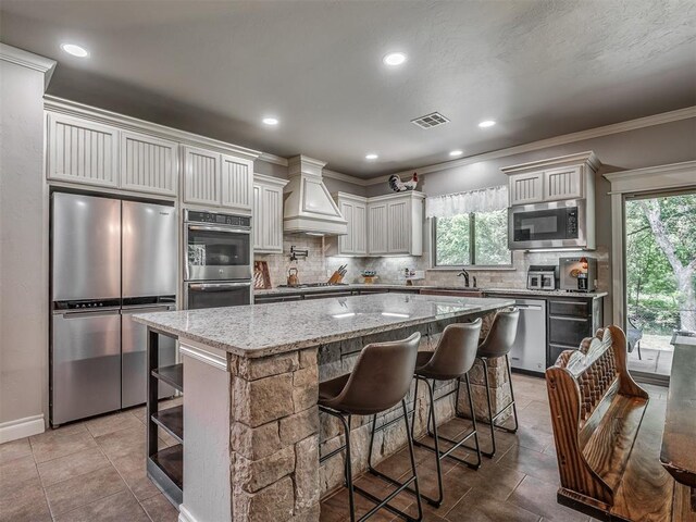 13505 Shady Pine Cir, Edmond, OK 73025 - kitchen featuring appliances with stainless steel finishes, premium range hood, decorative backsplash, a kitchen island, and ornamental molding