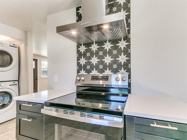 7624 NW 14th Ter, Oklahoma City, OK 73127 - kitchen with stainless steel electric stove, ventilation hood, stacked washer and clothes dryer, light wood-style flooring, and light countertops