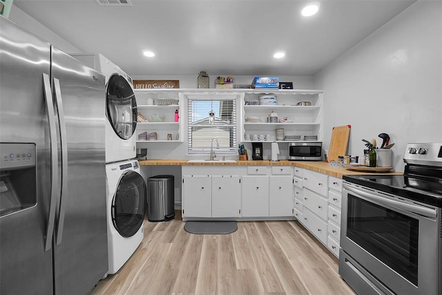 109 Cowan Ave, Fort Cobb, OK 73038 - kitchen with stainless steel appliances, estacked washer and dryer, open shelves, white cabinetry, and light wood-style floors