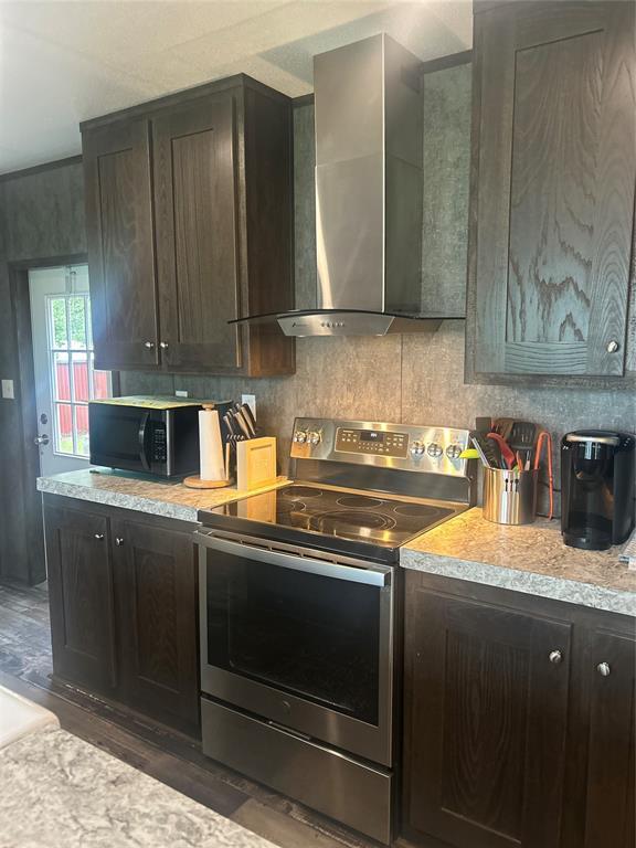 4341 Paradise Rd, Kingston, OK 73429 - kitchen with stainless steel electric stove, black microwave, wall chimney exhaust hood, wood finished floors, and decorative backsplash