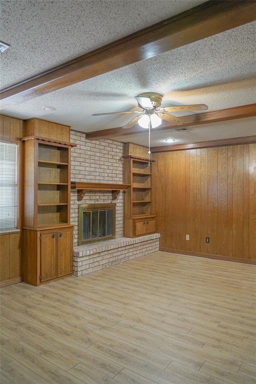 2313 SW 91st St, Oklahoma City, OK 73159 - unfurnished living room featuring a textured ceiling, a ceiling fan, wood walls, a brick fireplace, and light wood-type flooring